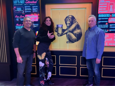 3 attendees posing with wall decor of monkey drinking beer